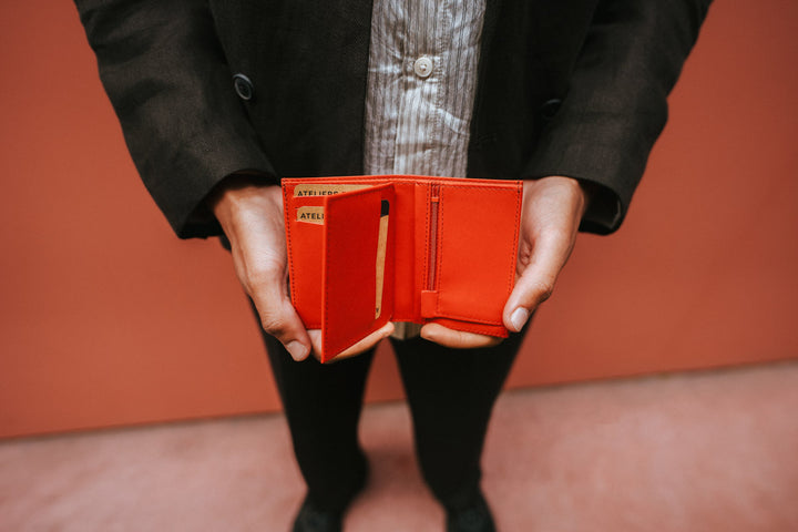 Portefeuille compact en cuir pleine fleur PLATON coloris orange, tenu en main – Ateliers Fourès